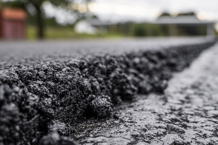A large layer of fresh hot asphalt. Layer of asphalt raw material in a shallow depth of field. Rollers rollin fresh hot asphalt on the new road. Road construction. Construction of a new road